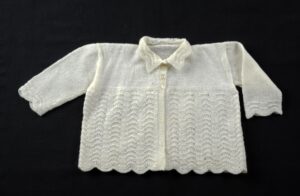 Childs matinee jacket with plain stockinette upper part and arms, wave pattern lower body and scalloped bottom.