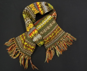 Fair Isle scarf with tassels. The background is browns and the motifs are green grey, red and yellow