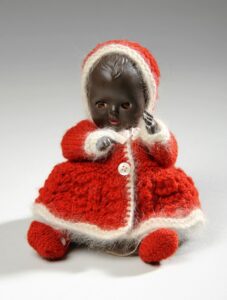 Doll in knitted red coat with white edging.