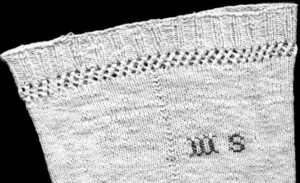 Top of knitted stocking with rib border and latticework below that above stocking stitch. Initials WS embroidered on.