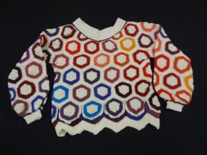 Knitted jumper with zig-zag bottom and overall design of hollow circles of blues, purple, browns, orange, yellow and red on a cream background