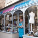 Owner of Crafts of Thirsk standing in shop doorway with example window displays on either side.