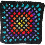 Photograph of lattice crochet with a black lattice and brightly coloured squares within it reminiscent of stained glass.