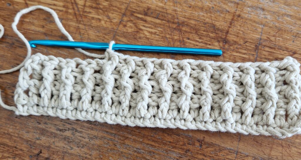 Partly completed swatch of cables made using crochet with the hook still attached