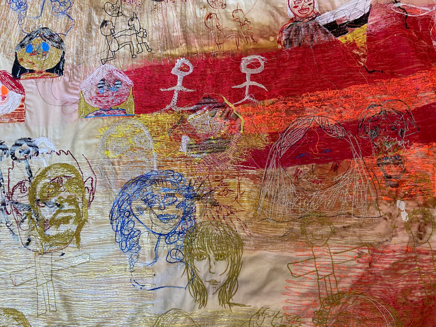 Photograph of a section of textile art with fabric dyed in broad stripes nd blocks with embroidered faces resembling sketches by children of varying ages.