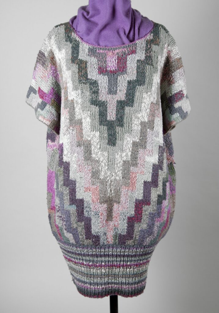 Multicoloured dress with geometric pattern of steped Vs. The bottom of the dress is drawn in by tight ribbing.
