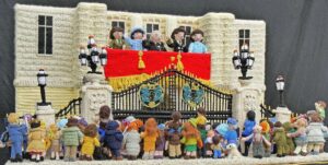 Knitted scene showing front of Buckingham Palace with the wartime Royal Family on the balcony watched by a celebrating public.
