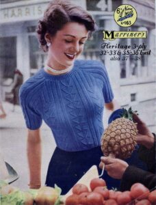 Cover of Marriner's pattern 163 showing a lady ar a fruit market being shown a pineapple. She is wearing a close fitting blue sweater with a geometric knit and purl pattern.
