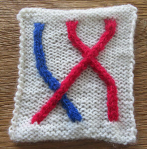 Knitted swatch showing crossing cables in blue and red.