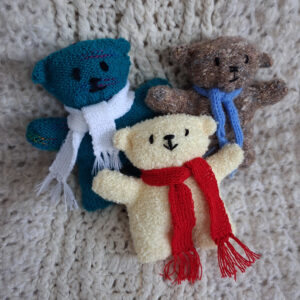 Blue-green, brown and yellow machine knit teddy bears wearing scarves.