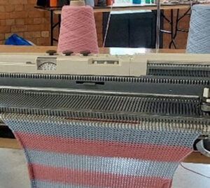Knitting machine with striped fabric being created.