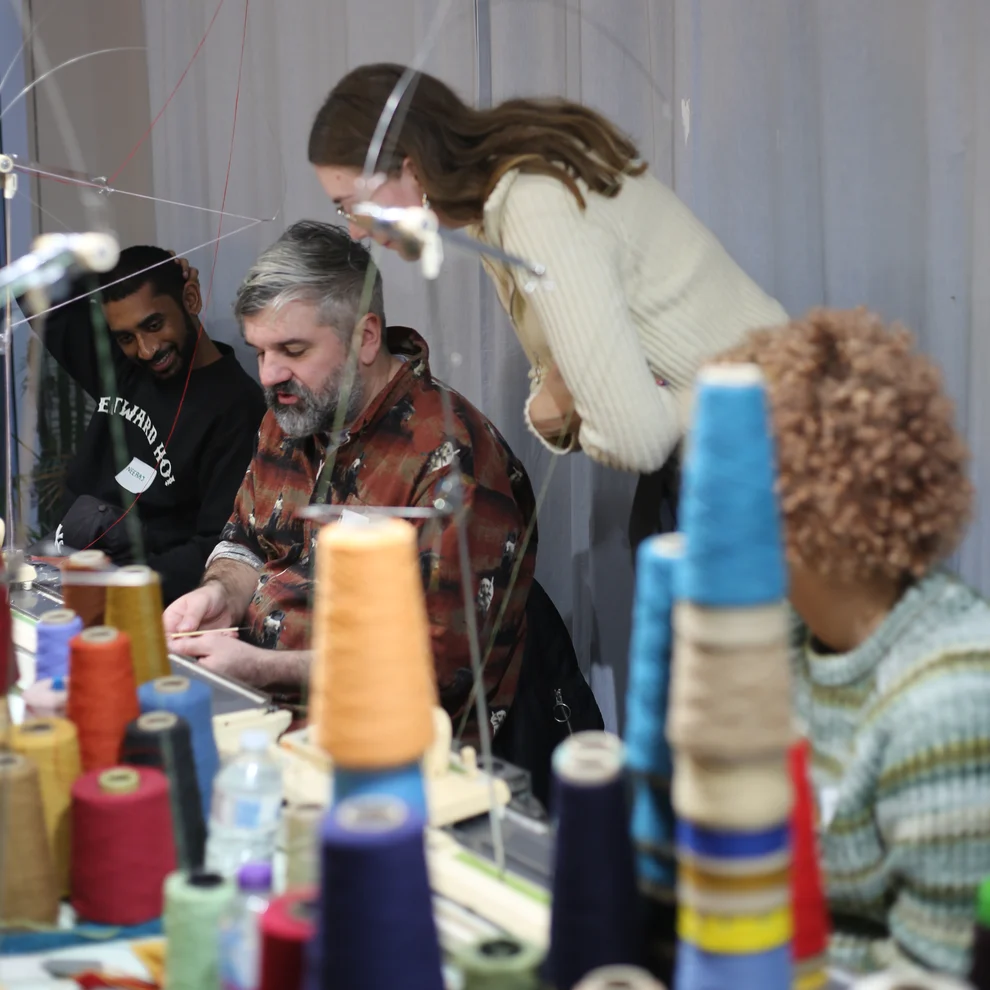 People sitting at knitting machine learning how to use it.